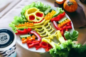 Photo of a skeleton made from vegetables on a plate. There is a pot of yogurt on the foreground.